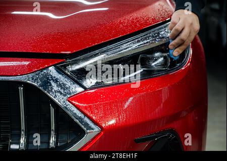 Un technicien lisse le film de vinyle sur un phare de voiture, éliminant les bulles d'air. Banque D'Images