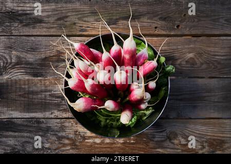 Bouquet de radis frais et entiers dans un bol sur une vieille table en bois, vu d'en haut, ambiance automnale. Banque D'Images