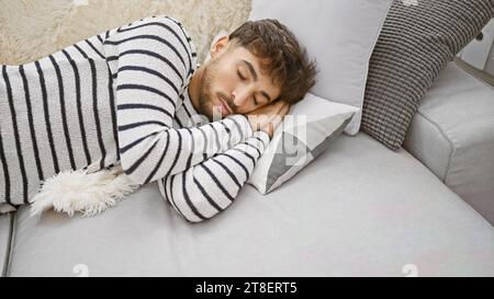 Beau jeune homme arabe, avec une barbe détendue, confortablement allongé sur son canapé confortable de salon, trouvant le confort à l'intérieur comme il tombe dans une profondeur Banque D'Images