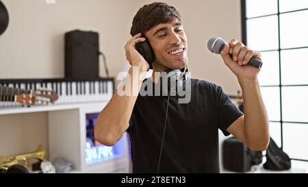 Confiant, jeune artiste hispanique chantant joyeusement son cœur dans un studio de musique, incarnant la mélodie de son âme Banque D'Images