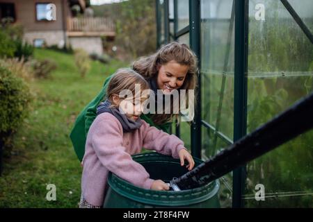 Fille et mère ramasser l'eau de pluie de barell sous le tuyau de descente. Concept de conservation de l'eau dans le jardin. Banque D'Images