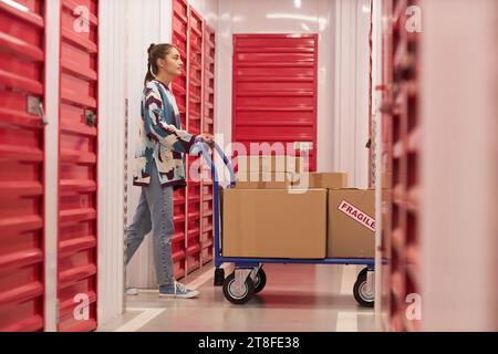 Jeune femme poussant le chariot avec des biens fragiles à l'unité de self-stockage Banque D'Images
