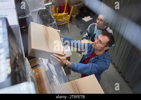 Couple mettant des boîtes emballées sur l'étagère dans l'unité de self-stockage qu'ils louent Banque D'Images