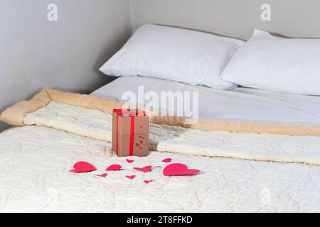 Cadeau de Saint-Valentin sur le lit avec literie blanche et amour rouge. Banque D'Images