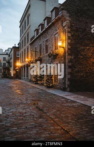 Une vieille rue pavée au crépuscule avec des lampadaires vintage et des lumières de vacances ornant des bâtiments pittoresques au Québec, Canada Banque D'Images