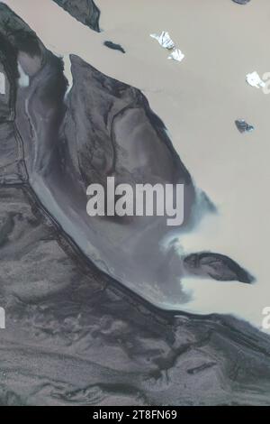 Un plan aérien de rivières glaciaires coulant à travers les cendres volcaniques et les sables près du glacier Vatnajokull en Islande avec de petits icebergs parsemant l'eau Banque D'Images