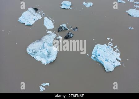 Vue du dessus de morceaux de glace et de rochers dispersés sur des eaux boueuses présentant une vue rapprochée d'une eau de fonte glaciaire au parc national de Vatnajokull Banque D'Images