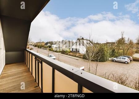 Vue des voitures garées sur la rue et les maisons en rangée avec des plantes contre le ciel nuageux vu à travers le balcon moderne vide Banque D'Images