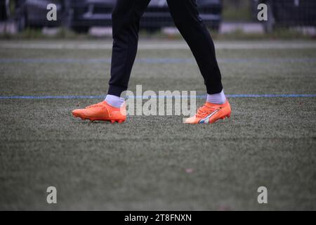 Joueur de football masculin portant des crampons orange vif et noirs, debout dans une position prête avec les pieds fermement plantés sur le sol Banque D'Images