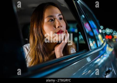 En traversant les rues nocturnes de la ville, la femme dans la voiture regarde par la fenêtre sur le paysage Banque D'Images