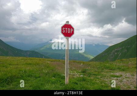 Panneau d'arrêt rouge contre le sommet des montagnes et les chaînes sous les nuages bas. Jour, été. Voie de choix ou concept de réchauffement climatique. Photo de haute qualité Banque D'Images