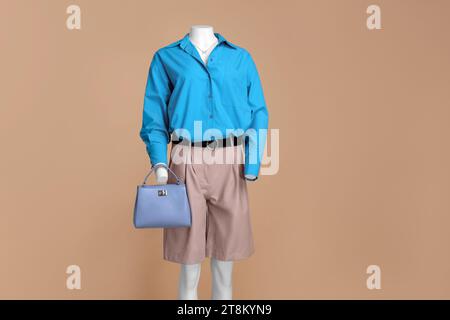 Mannequin femme habillé de shorts en cuir et chemise bleu clair élégant avec accessoires sur fond beige Banque D'Images