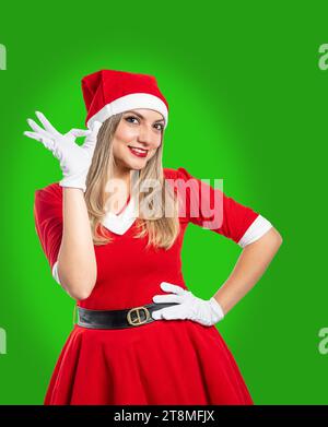 Jeune père noël faisant le geste ok avec sa main souriant regardant la caméra sur fond vert. concept de noël Banque D'Images