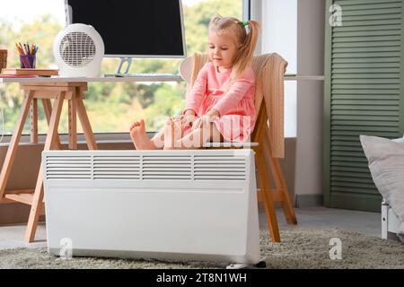 Pieds nus petite fille réchauffant les jambes près du radiateur à la maison Banque D'Images