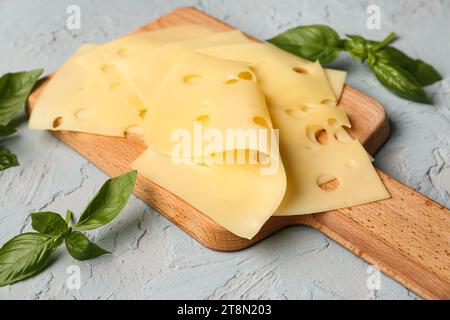 Planche avec des tranches de fromage savoureuses et des feuilles de basilic sur fond clair, gros plan Banque D'Images