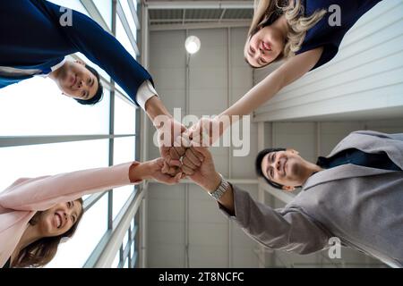 Concept de team building. Collègue debout en cercle cognant le poing ensemble, célébrant le succès de l'entreprise dans un bureau moderne avec haut plafond. Vue de dessous Banque D'Images