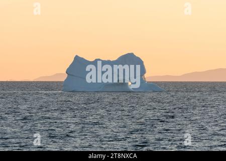 Un iceberg flotte dans le soleil levant du matin au large des montagnes de la côte groenlandaise. Baie de Disko, Groenland occidental, Danemark Banque D'Images