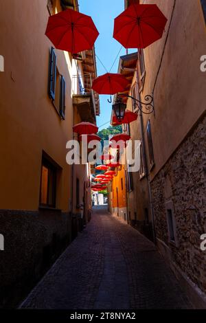 Rue de la ville à Porto Ceresio avec parasols suspendus dans une journée d'été ensoleillée à Porto Ceresio, Lombardie, Italie Banque D'Images