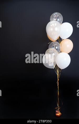 Sur un fond noir, des ballons de nuances claires - blanc, beige, transparent - volent. Espace pour le texte Banque D'Images