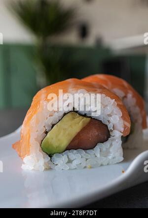 Une image rapprochée de rouleaux de sushi fraîchement préparés, avec des tranches fraîches de thon et d'avocat, servis sur une assiette blanche Banque D'Images