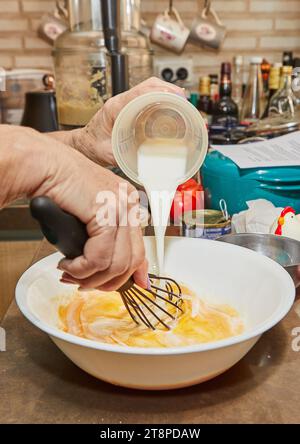 Le chef verse le lait de la tasse à mesurer dans les œufs fouettés Banque D'Images