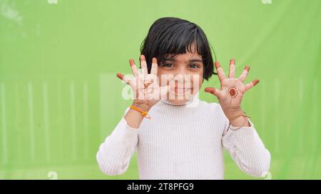 Ravi positif belle petite fille caucasienne portant une robe blanche sur fond vert ouvre la bouche et les bras paumes vers le haut après avoir eu un grand résultat Banque D'Images