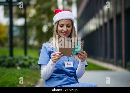 Infirmière avec chapeau de noël sur la tête lisant la carte de noël du patient enfant. Travailler à l'hôpital le jour de Noël. Femme médecin travaillant un Noël Banque D'Images