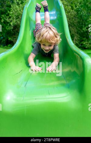 Un petit garçon monte sur le ventre sur un toboggan Banque D'Images