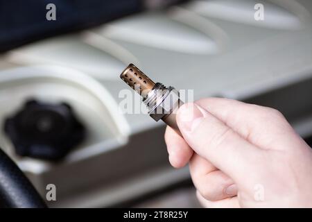 Capteur d'oxygène pour moteurs à essence et diesel dans la main contre moteur de voiture. Le mécanicien tient le capteur d'oxygène. sonde lambda. Banque D'Images