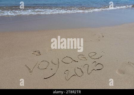 L'inscription voyaje 2022 en français, Voyage 2022, sur le sable par l'eau et la vague montante, mer vacances plage au bord de la mer. Banque D'Images