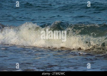 Une grande et forte onde de tempête de couleur turquoise avec des éclaboussures de mousse blanche coule et se brise sur le rivage. Banque D'Images