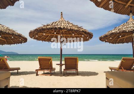 Parasols en paille et transats sur la plage de galets vide avec mer en arrière-plan Banque D'Images