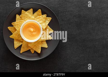 Nachos sur assiette grise et salsa au fromage, sur fond sombre, vue de dessus, espace pour copier le texte. Banque D'Images