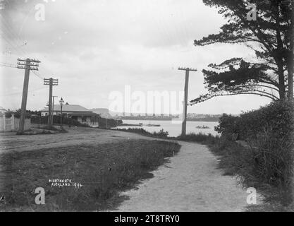 Vue de Fraser's Corner, Northcote, vue vers Auckland, Nouvelle-Zélande, vue vers le sud vers Northcote Wharf avec Auckland, Nouvelle-Zélande au loin. À gauche se trouve une maison surplombant Little Shoal Bay et le port de Waitemata. Un homme peut être vu marchant sur la route vers la caméra. Une clôture de piquet blanche, des lignes électriques et une lampe à gaz peuvent également être vus sur le côté gauche. Un ferry approche de Northcote Wharf. Prise ca 1910 d'Auckland, Nouvelle-Zélande Banque D'Images