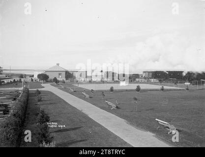 Victoria Park, Thames, vue sur Victoria Park vers l'ouest. Montre des arbres récemment plantés, des bancs de parc en fer forgé, chemin en béton, et des courts de tennis ?. Sur le côté gauche se trouve une cour à bois. Au-delà des cours se trouve une maison et une dépendance ; aussi un train et des voitures. La mer peut être vue au loin sur la gauche. Photographie prise au début des années 1900 Banque D'Images