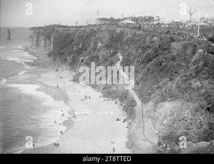 Cape Foulwind, vue regardant vers le bas sur une plage depuis le sommet d'une falaise à Cape Foulwind, regardant vers le nord. Montre les falaises et le littoral. Les gens sont sur la plage, et marchent sur un chemin menant vers le bas de la colline. Au sommet de la falaise se trouve une zone de loisirs, où les gens se rassemblent., entre 1900 et 1920 Banque D'Images