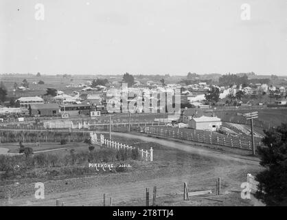 Vue générale de Pukekohe, vue de Pukekohe regardant à travers une intersection, à une zone clôturée et des arbres nouvellement plantés (clôturés) vers les gares de triage à mi-distance et le canton de Pukekohe au-delà. L'hôtel Pukekohe (avec son nom sur le toit) est sur la gauche. Photographie prise vers 1910 Banque D'Images