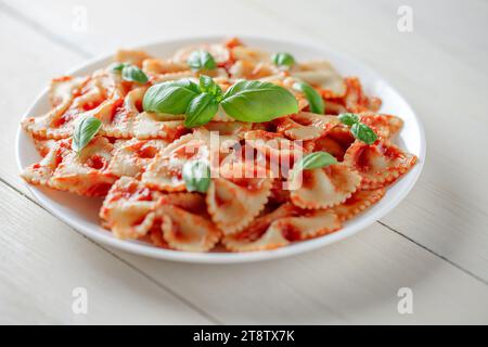 Pâtes Farfalle cuites avec sauce tomate et basilic, dans une assiette blanche, mise au point sélective. Banque D'Images
