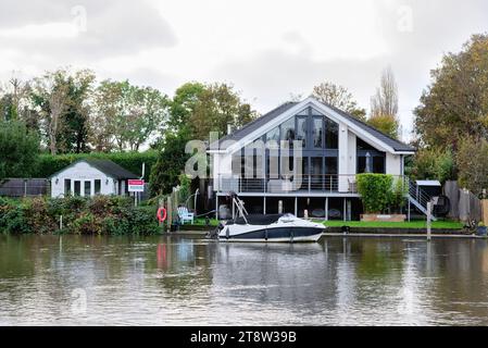 Une maison de style très moderne sur le bord de la rivière à Laleham Reach avec un petit bungalow en bois délabré à vendre adjacent à elle, Staines Angleterre Royaume-Uni Banque D'Images