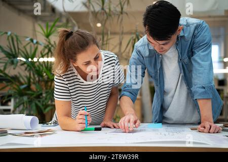 Vue de face des architectes s'appuyant sur la table tout en travaillant sur les plans Banque D'Images