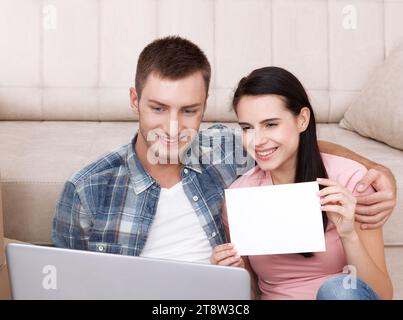 Belle jeune couple communique en vidéo chat. Une femme est souriant et montrant une feuille de papier vierge. Banque D'Images