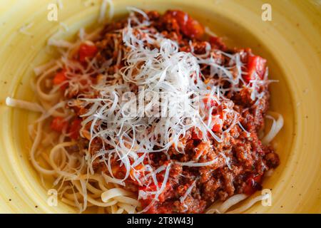 Pâtes bolognaises parsemées de parmesan râpé dans une assiette jaune profonde, mise au point sélective Banque D'Images