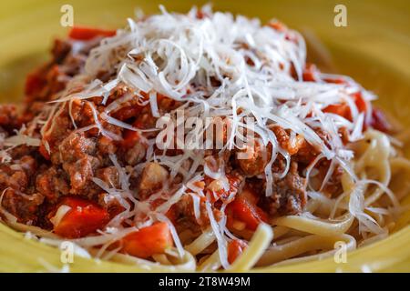 Pâtes bolognaises parsemées de parmesan râpé dans une assiette jaune profonde, mise au point sélective Banque D'Images