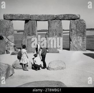 Années 1960, historique, les gens à côté des anciennes pierres de sarsen dans les célèbres monuments préhistoriques de Stonehenge situés sur la plaine de Salisbury, à Amesbury, Wiltshire, Angleterre, Royaume-Uni. En 1986, les visiteurs du monument n'ont pas été autorisés à errer librement parmi les pierres comme avant, en raison de craintes d'érosion. Banque D'Images