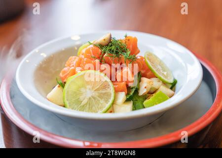 Saumon tranché épicé avec salade de fruits dans un bol en céramique blanche. Plat à amuse-gueule de fusion Banque D'Images