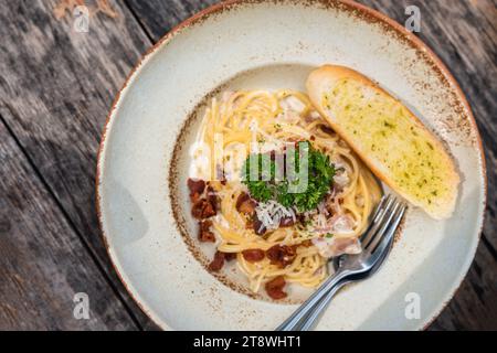Vue de dessus de Spaghetti Carbonara avec jambon croustillant et sauce à la crème blanche dans une assiette en céramique sur une table en bois dans un restaurant italien Banque D'Images