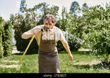 jardinier barbu en tablier de lin buvant de l'eau du tuyau après avoir travaillé dans le jardin, photo candide Banque D'Images