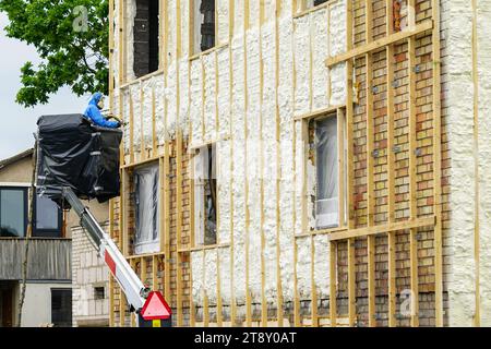 Technicien pulvérisant la couche de mousse d'isolation thermique sur le mur extérieur d'une maison d'habitation en utilisant le pistolet à plusieurs composants pour la mousse de polyuréthane Banque D'Images