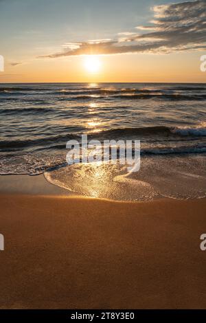 Un magnifique coucher de soleil sur une plage de sable. Le soleil se couche sur l'océan, projetant une lueur dorée sur l'eau et le sable. Banque D'Images