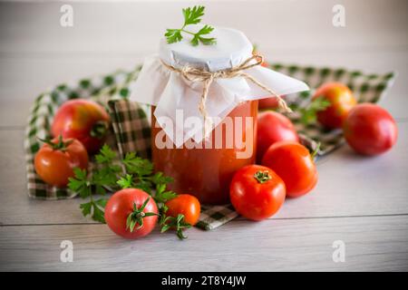 Jus de tomate maison cuit en conserve dans un pot de tomates naturelles, sur une table en bois. Banque D'Images